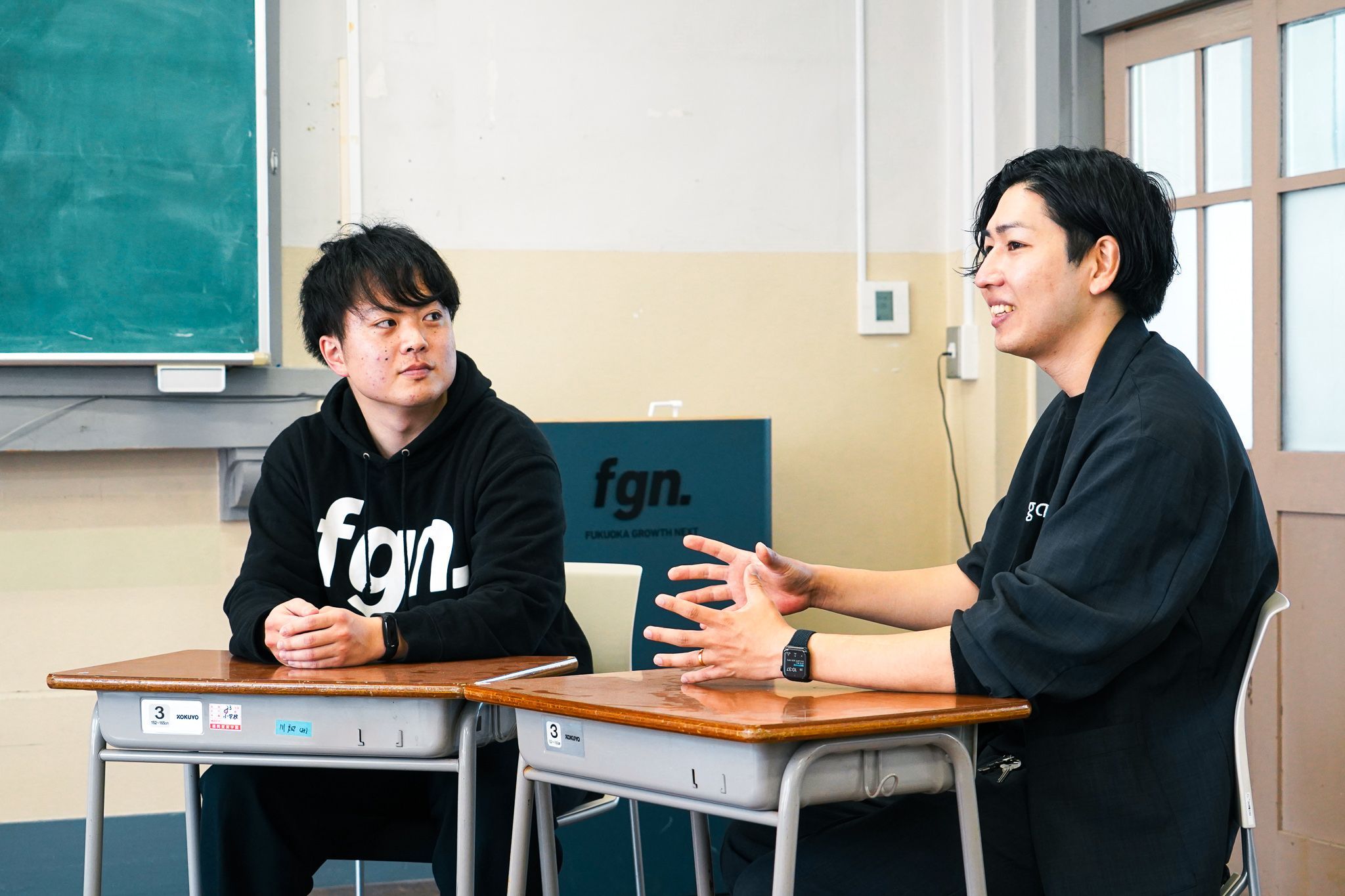 生徒用机に手を乗せ、ろくろ回しをするように身振り手振りで説明する吉岡さんと、吉岡さんを見つめる前山さん