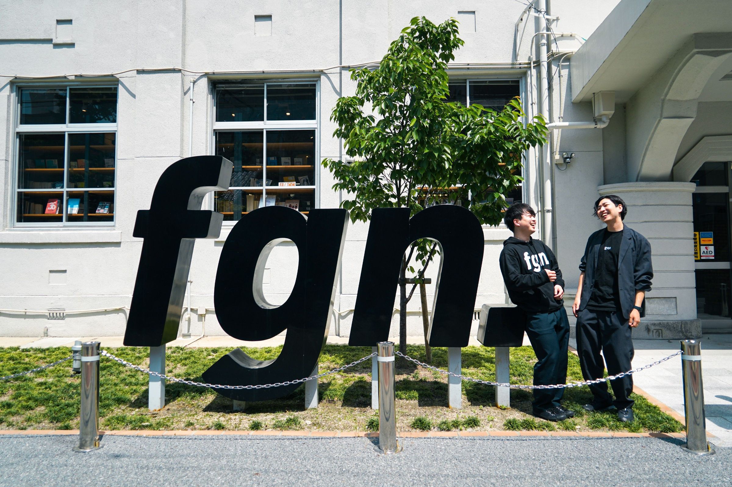 FGNの入り口横にある「fgn.」をかたどったオブジェの右側に立ち、談笑する崎山さんと、吉岡さん。