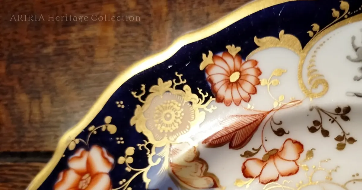 アンティーク皿の縁に描かれた金彩と花文様。その奥に、かすかに見える小さなライオンのモチーフ