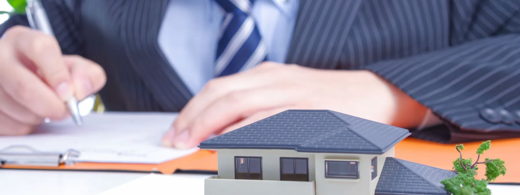 書類に記入する手とテーブル上の住宅模型