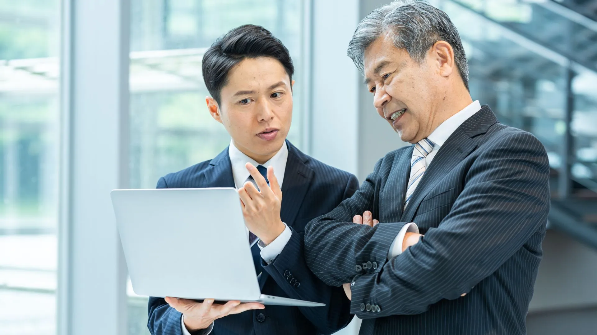 ラップトップを開いてエグゼクティブに説明をする人物、エグゼクティブはあまりの力ではなく、渋い顔をしている。