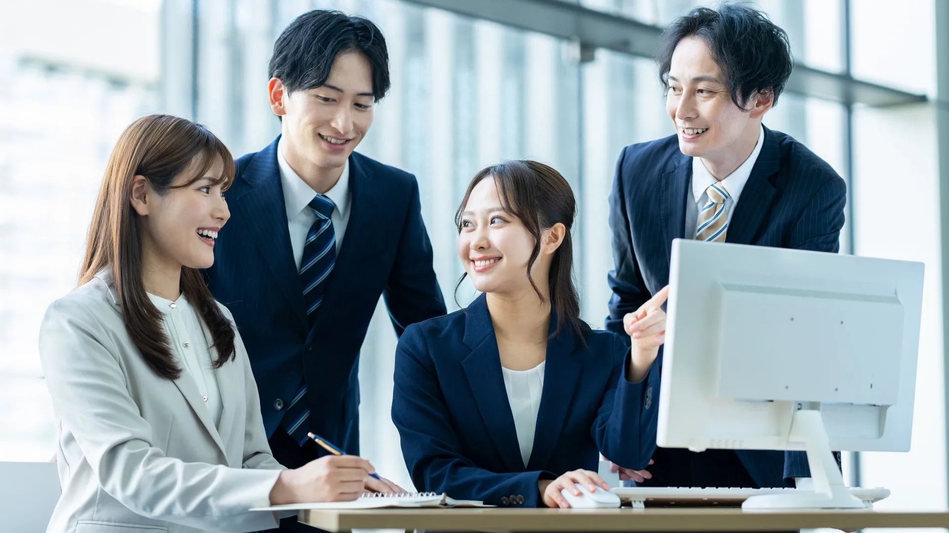 パソコンを前に情報をシェアする４人のビジネスパーソン。