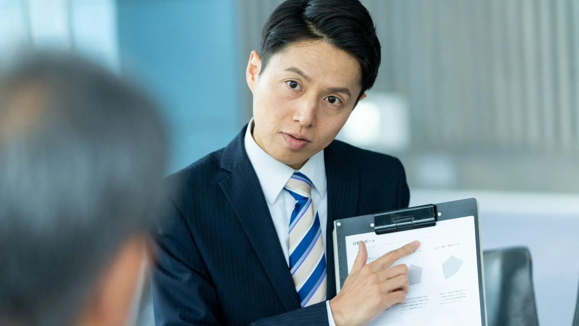 顧客に資料を見せながら説明をするビジネスパーソン。仮説シナリオを使って説明をするイメージ。