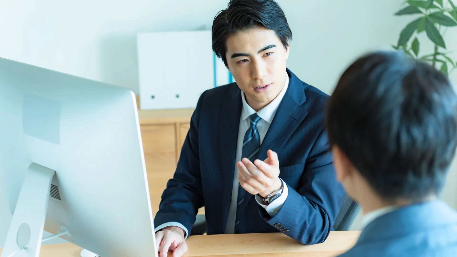 オフィスで上司が画面を見ながら、部下に検討ポイントを説明している場面