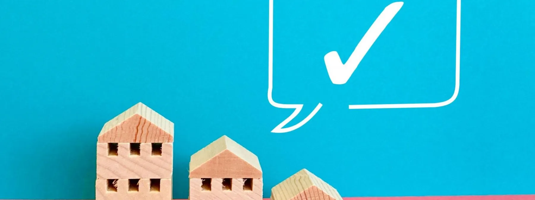 木製のミニチュア住宅とチェックマークが描かれたシンプルな背景