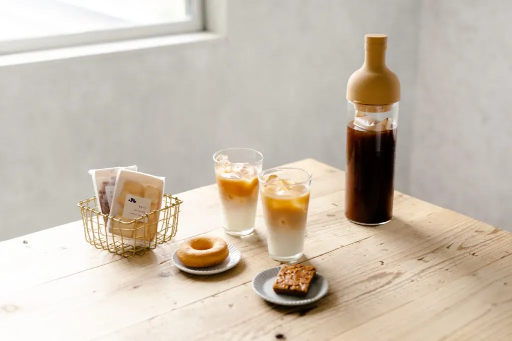 スナックミーのお菓子、カフェラテの注がれたグラス、アイスコーヒーのボトルなどが並べられたテーブル
