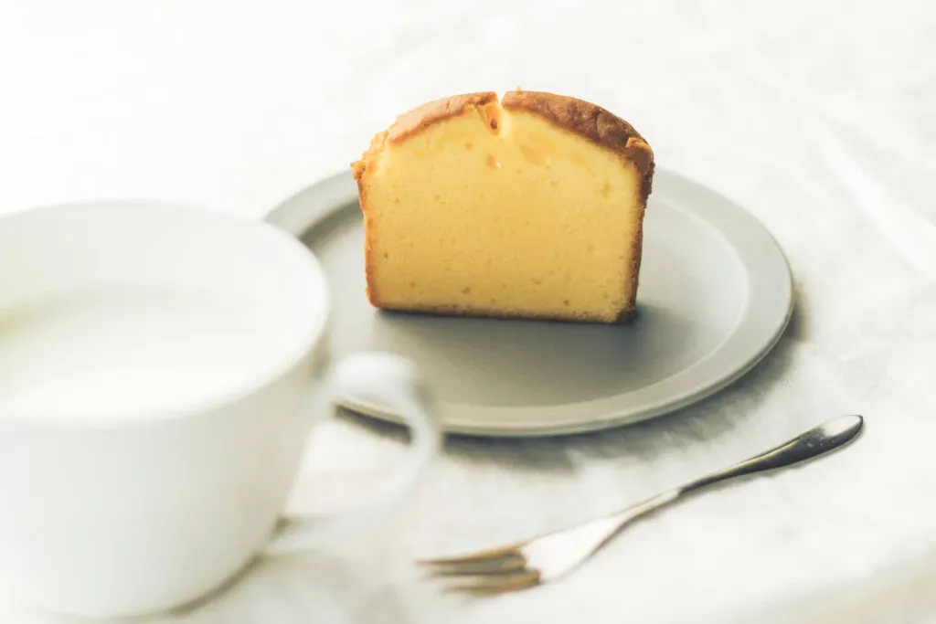 お皿に乗せられたスナックミーのパウンドケーキと、そばに置かれたティーカップ・カトラリー