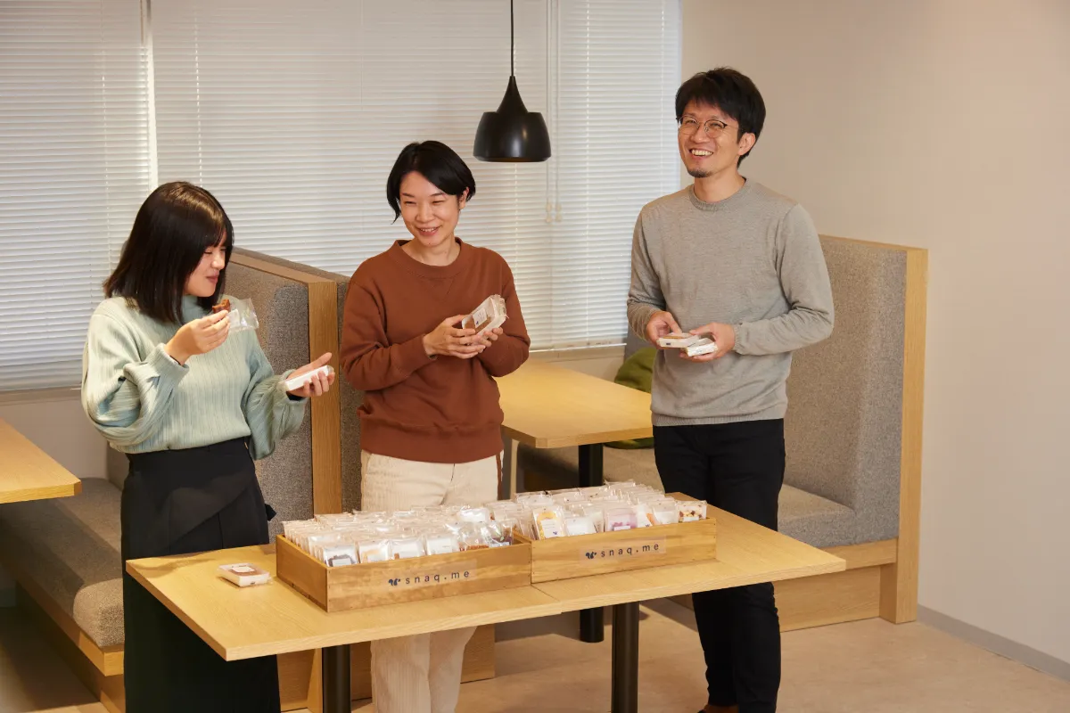 会社に導入されたスナックミーのおやつを手に談笑する男女3人