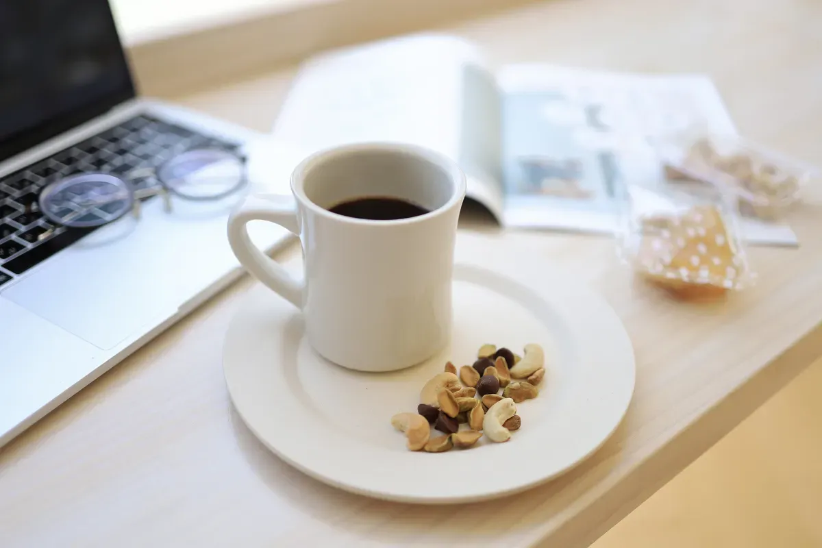 ノートパソコンのそばにコーヒーカップやスナックミーオフィスのお菓子が置かれた様子