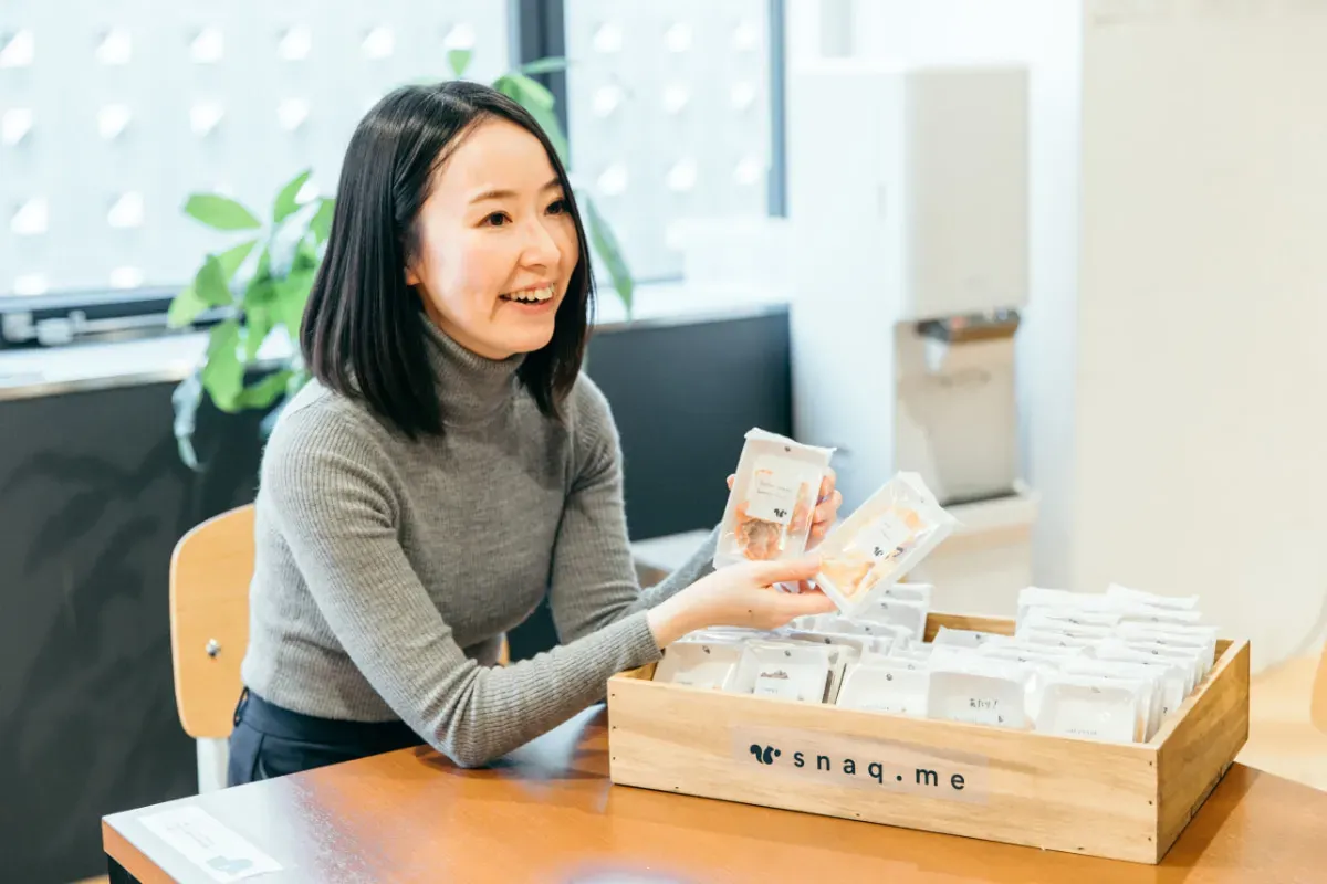 スナックミーのお菓子を手に持つ 『株式会社Zehitomo』のインタビューご担当者さま
