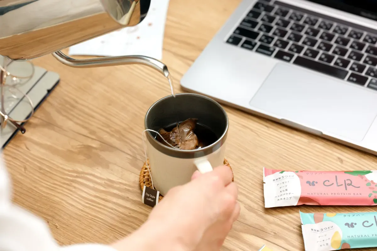 オフィスデスクでカップにお湯を注ぎ、ティーバッグ型のコーヒーを淹れている様子