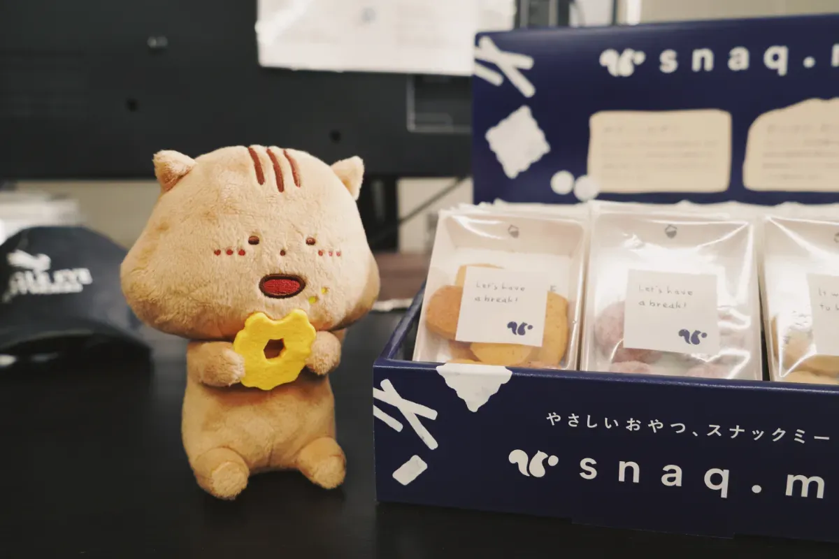 スナックミーオフィスの置き菓子の什器と、スナックミー社のマスコットキャラクターのぬいぐるみ