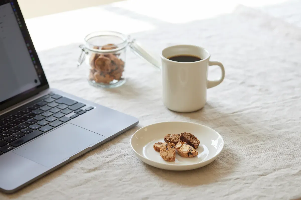 ノートパソコン、スナックミーオフィスのお菓子のお皿、コーヒーカップなどが並ぶテーブル
