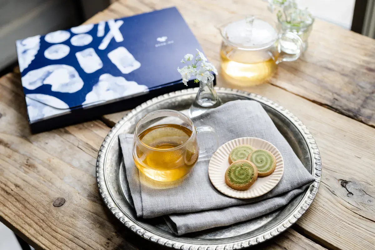 お茶とクッキーが乗ったシルバートレイ、スナックミーのお菓子の箱、ティーポットが置かれたテーブル