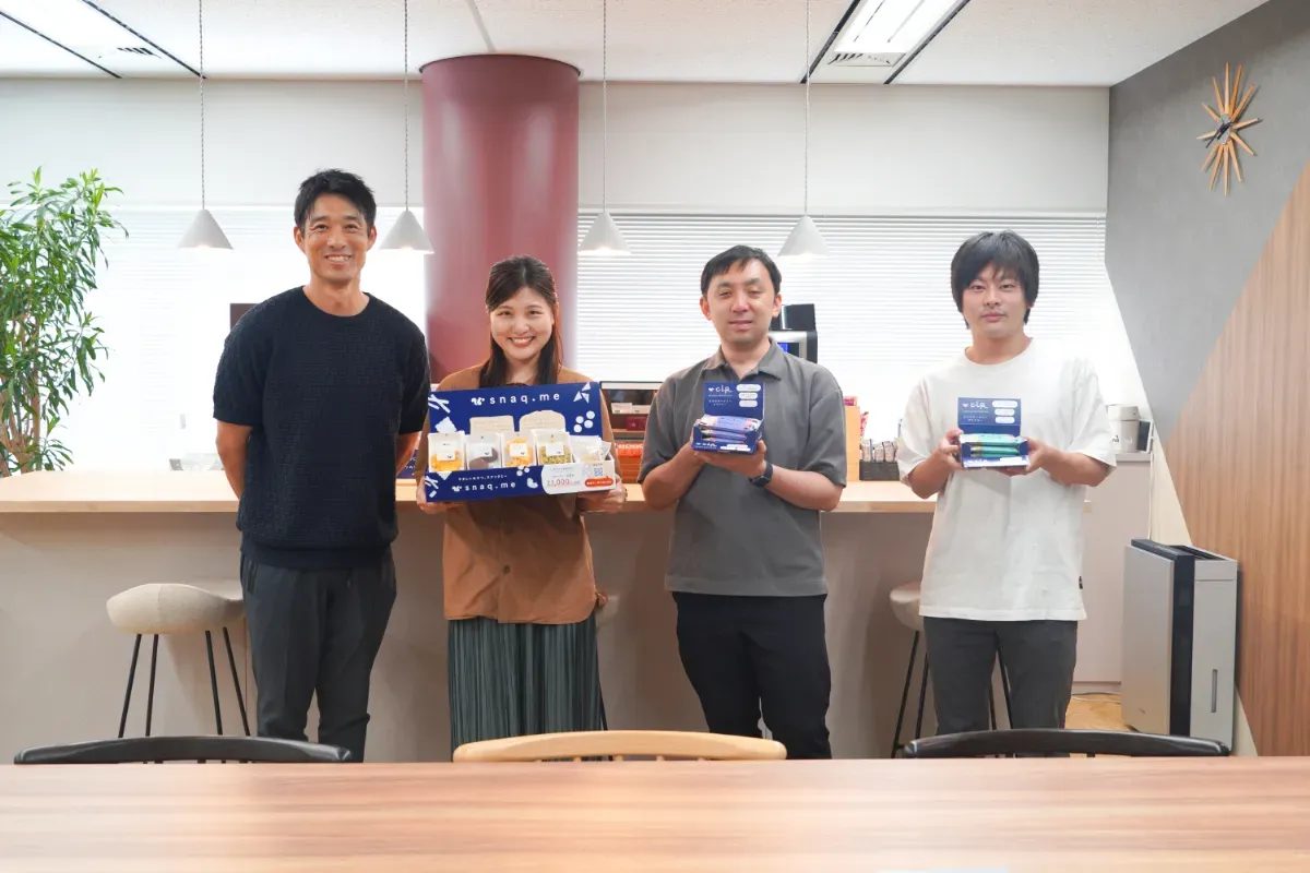 スナックミーオフィス導入企業『日本インフォメーション株式会社』さまのスタッフが、スナックミーのお菓子を盛った集合写真