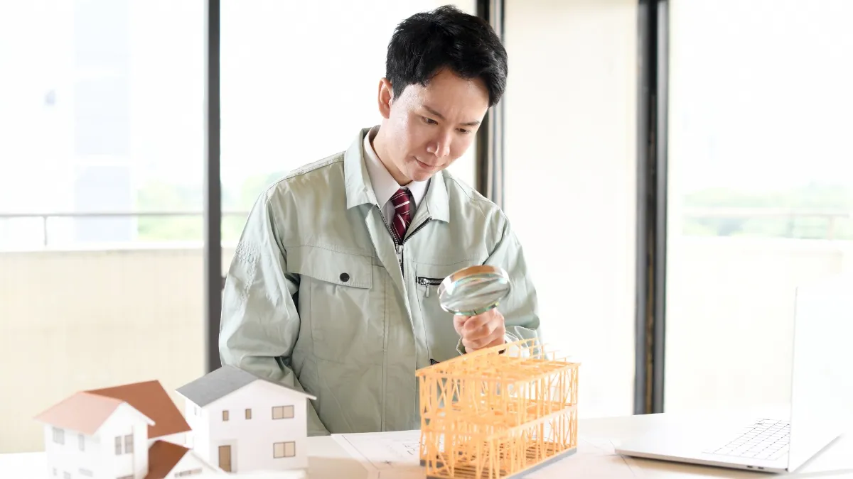 虫眼鏡で建築模型を覗く作業服姿の男性