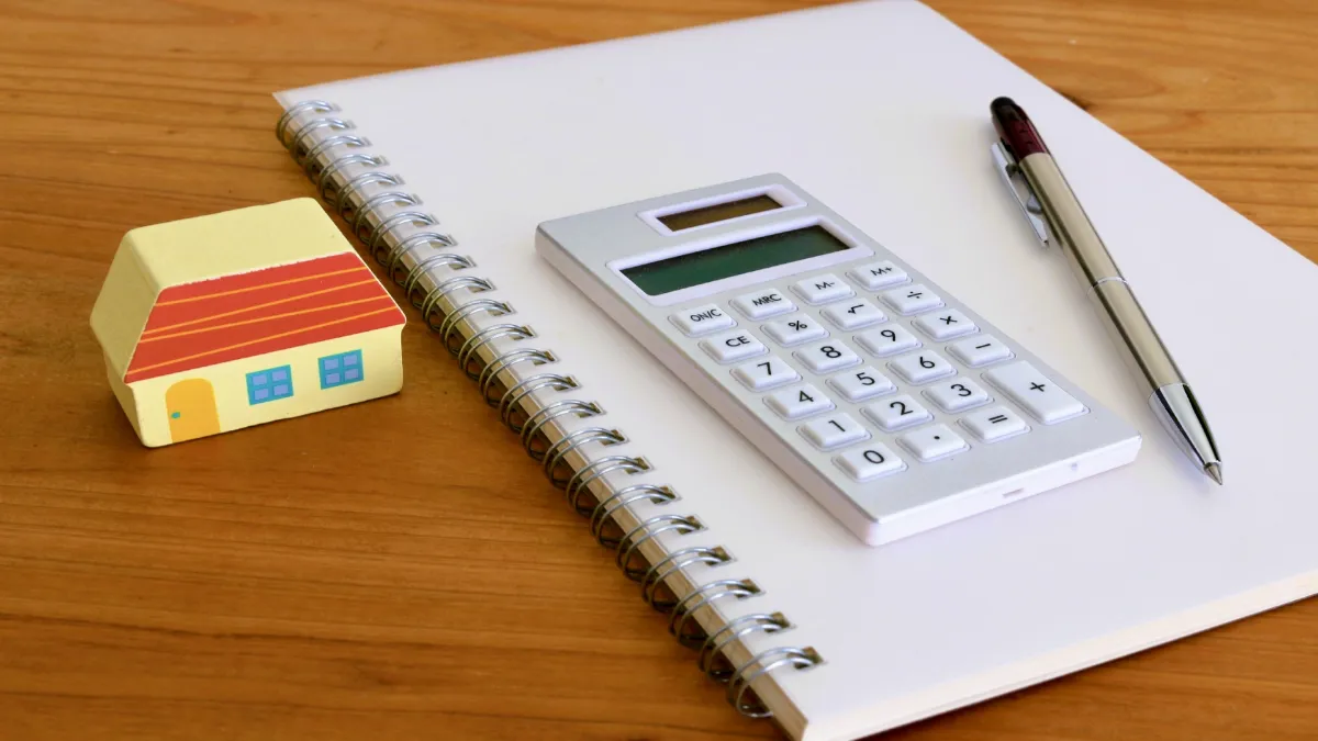 家の置物と電卓、ノートの写真が置かれている様子