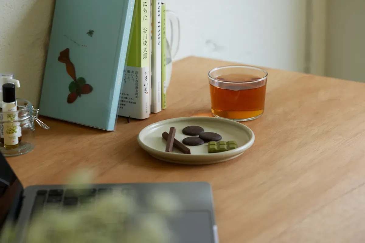 ノートパソコン、書籍、チョコレートの盛られた皿、お茶のグラスなどが並ぶテーブル