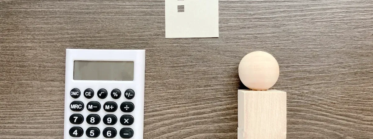 木製の机の上に白い電卓と木製の家、人物を模したオブジェが整然と並んでいる。