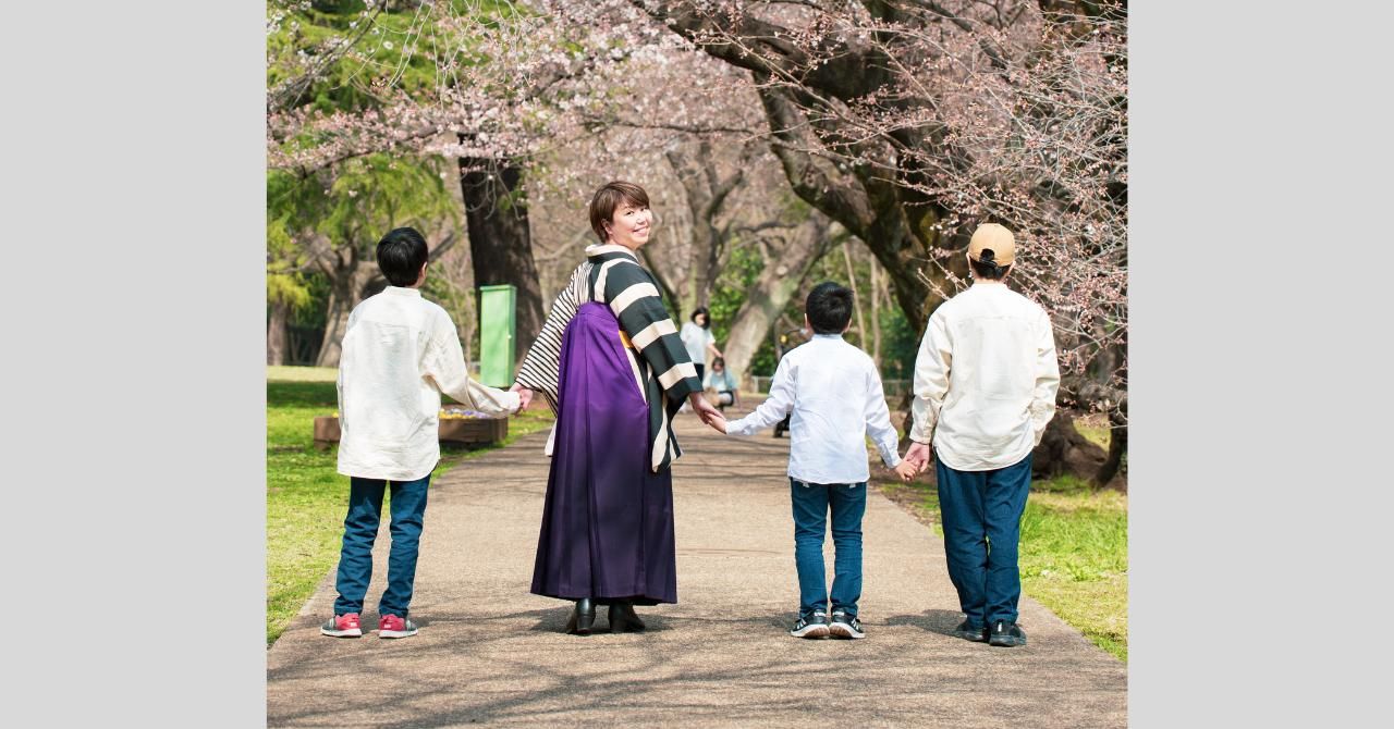 桜の下を手をつないで歩く親子