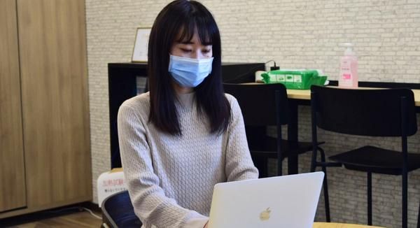 オフィスで机に座りMacBookに向かうマスクをした女性