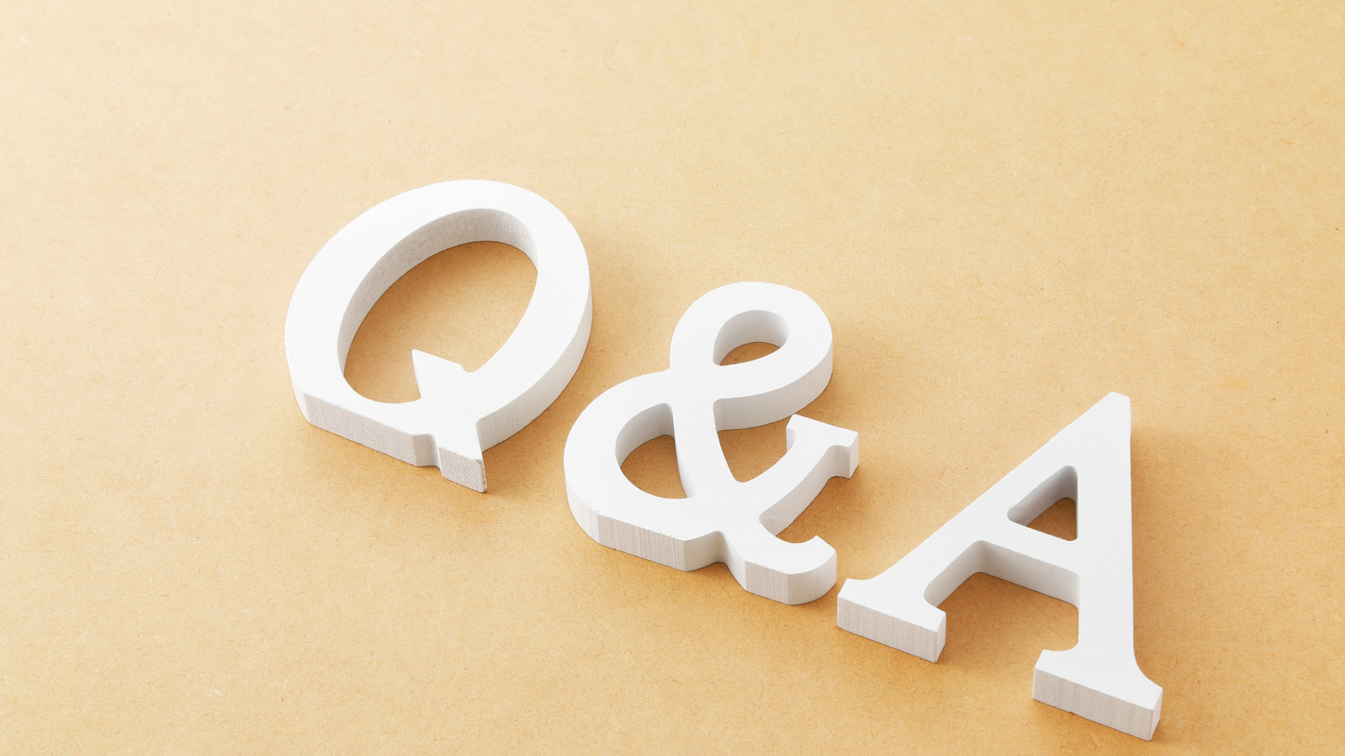 ベージュの背景に置かれた白い木製ブロックの「Q&A」の文字