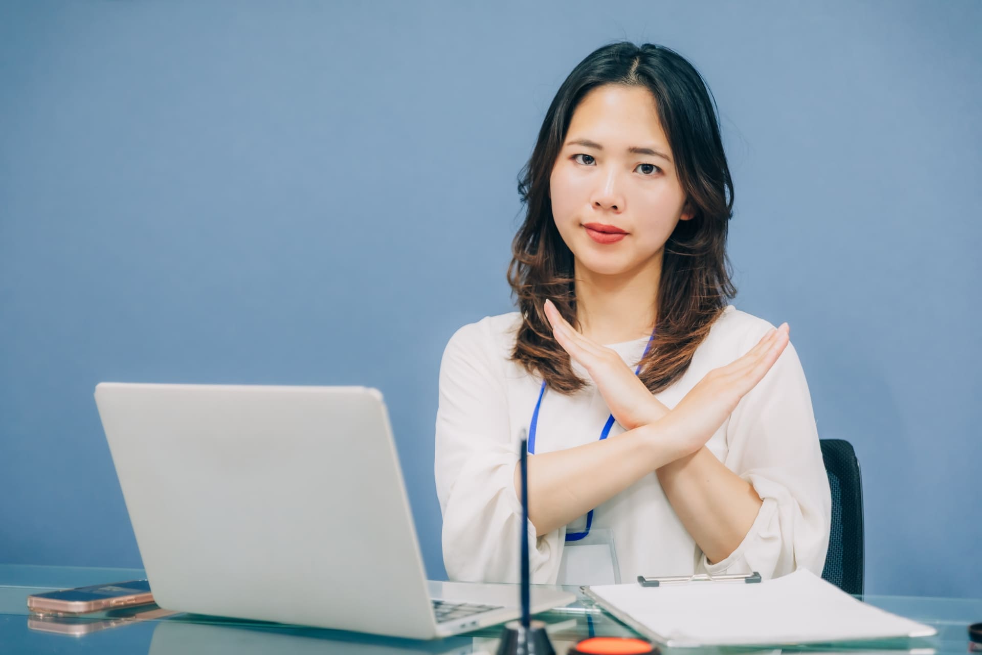 パソコンに向かう女性、手でバツポーすをしている画像