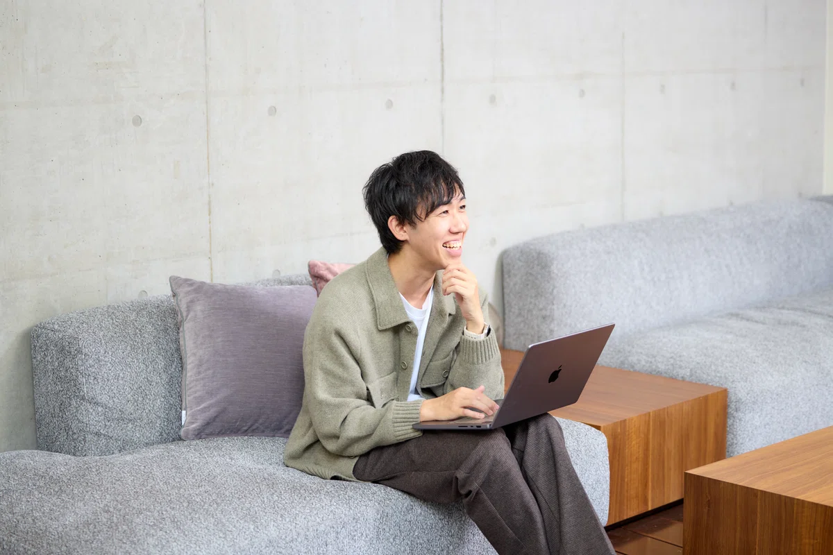 写真。顎に手を当て、質問に笑顔で応じるKamiyamaさん。