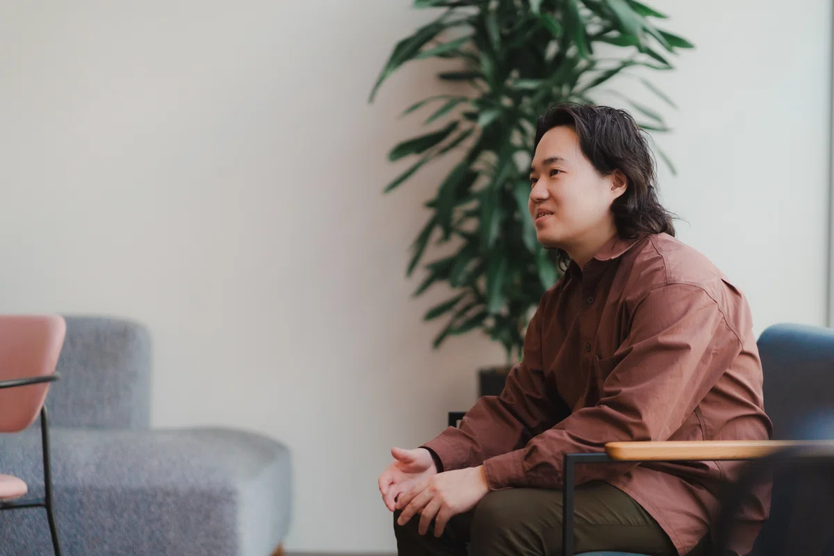 写真。腕を膝に置き、目線をインタビュイーに向けながら話すFumitoさん