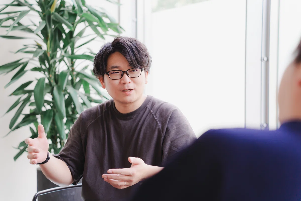 写真。ろくろを回すかの如く身振り手振りを交えながら、インタビュイーに説明をするMurakamiさん