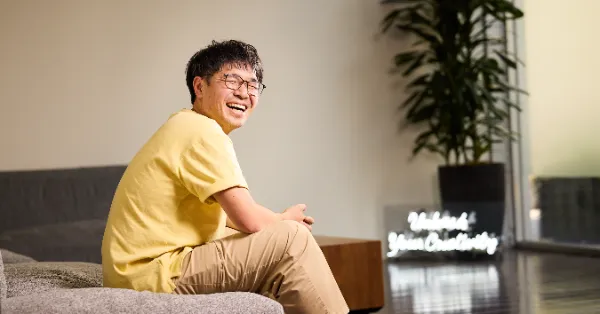 写真。ソファに腰掛け、笑顔でインタビューに応じるCTOのmorotaさん。黄色いシャツも相まって、朗らかな様子