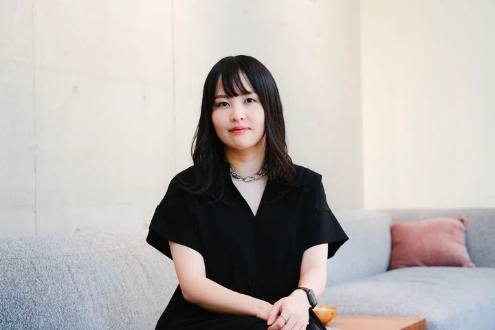 写真。ソファに腰掛けカメラの方を向くSakinoさん。