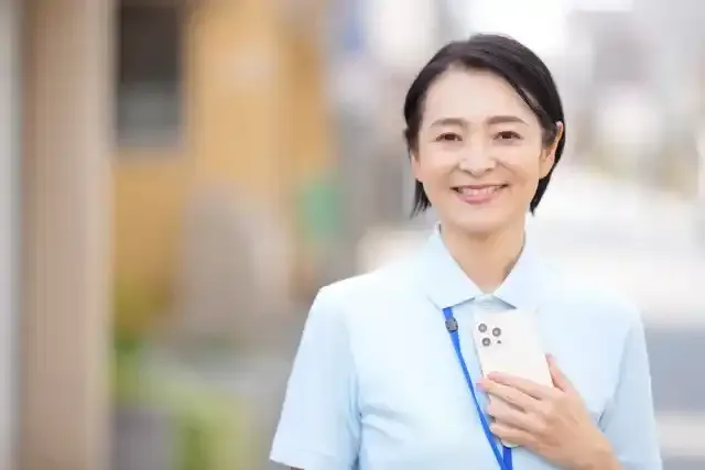 屋外でスマートフォンを持って立つ女性介護士