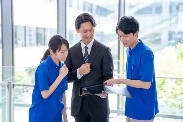 タブレットを見せるスーツの男とそれをみる男女