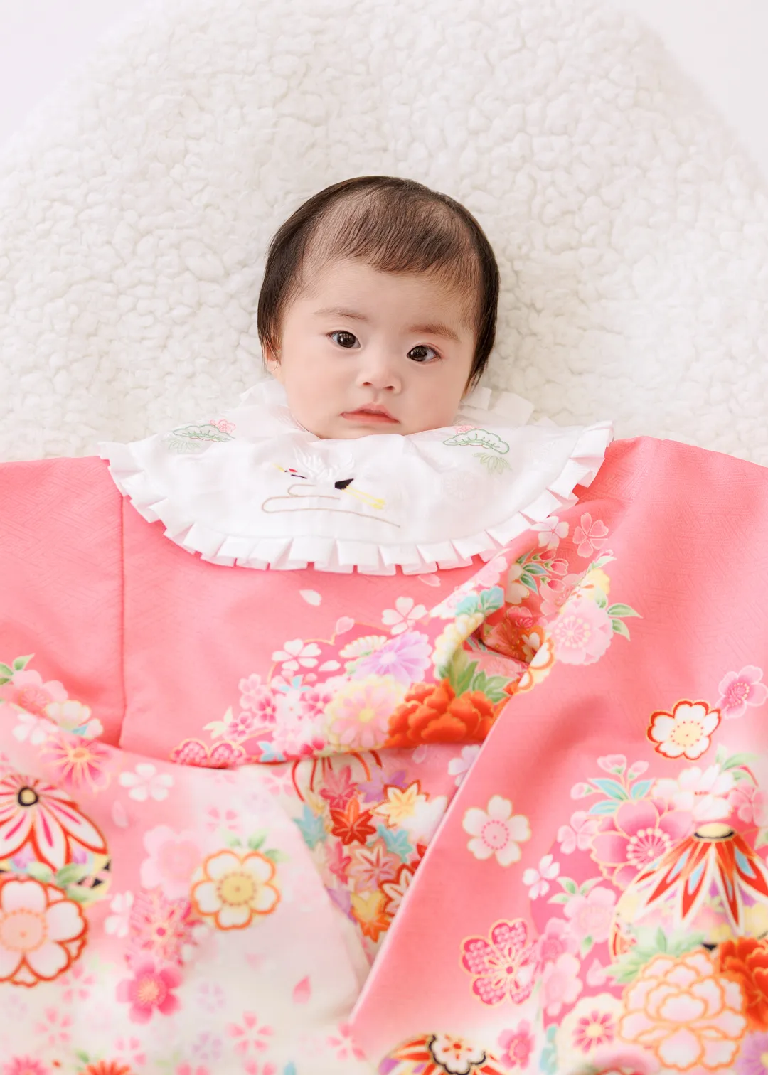 ピンク色の花柄祝い着姿で白いラグの上に横たわる女の子の百日祝いフォト(金沢市)|ヤマダフォト