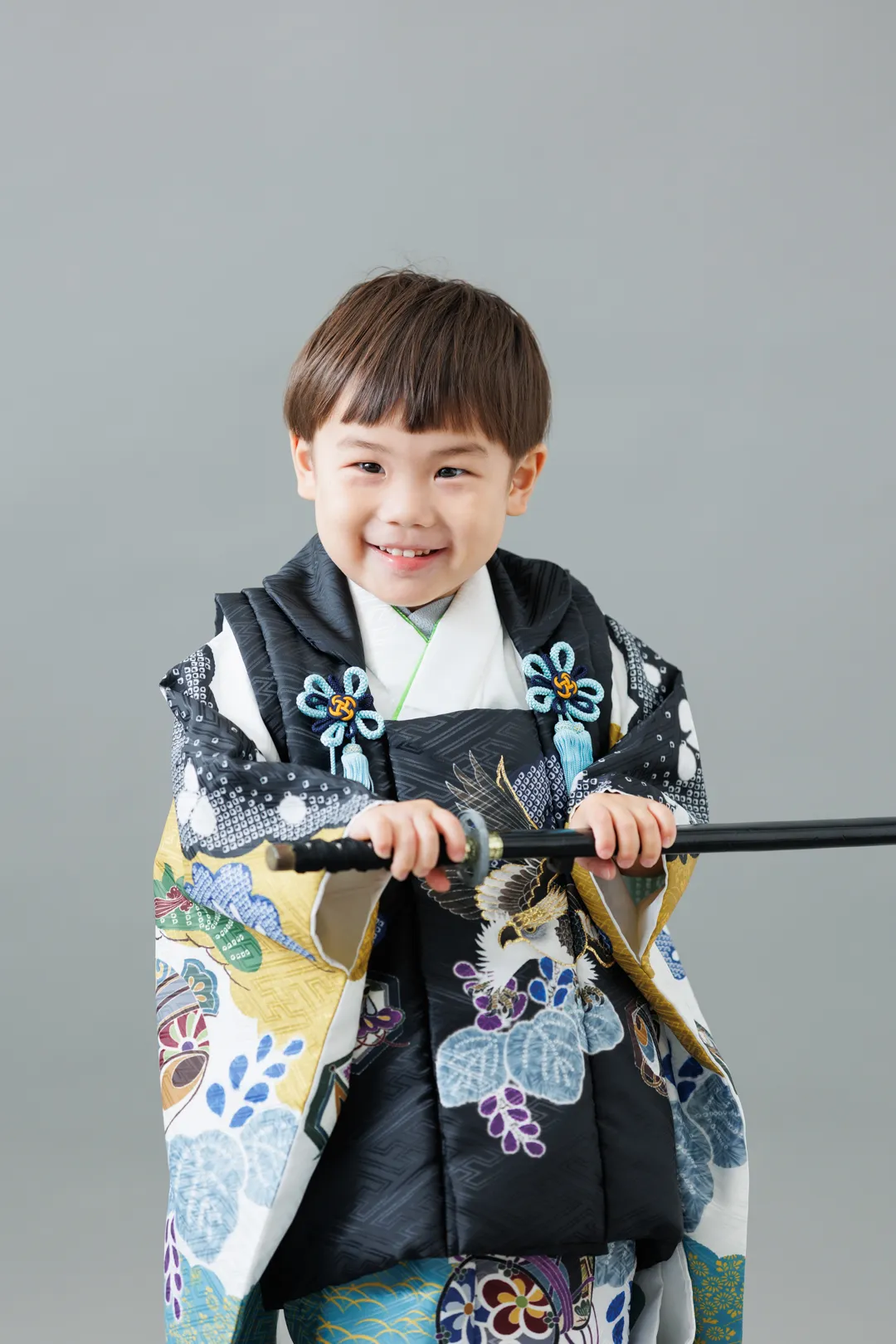 灰色のスタジオ背景で刀を手に笑顔を見せる花柄の袴姿の男の子（能美市）｜ヤマダフォト