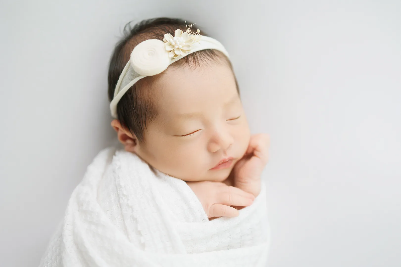 白いおくるみに包まれ花の髪飾りをつけた新生児の女の子のニューボーンフォト(野々市市)|ヤマダフォト