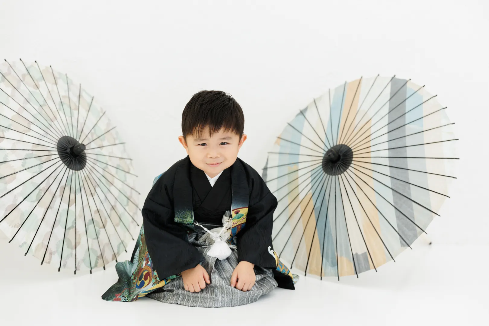 黒い着物袴姿で和傘2本を背景に座る男の子の七五三フォト(埼玉県川口市)|ヤマダフォト