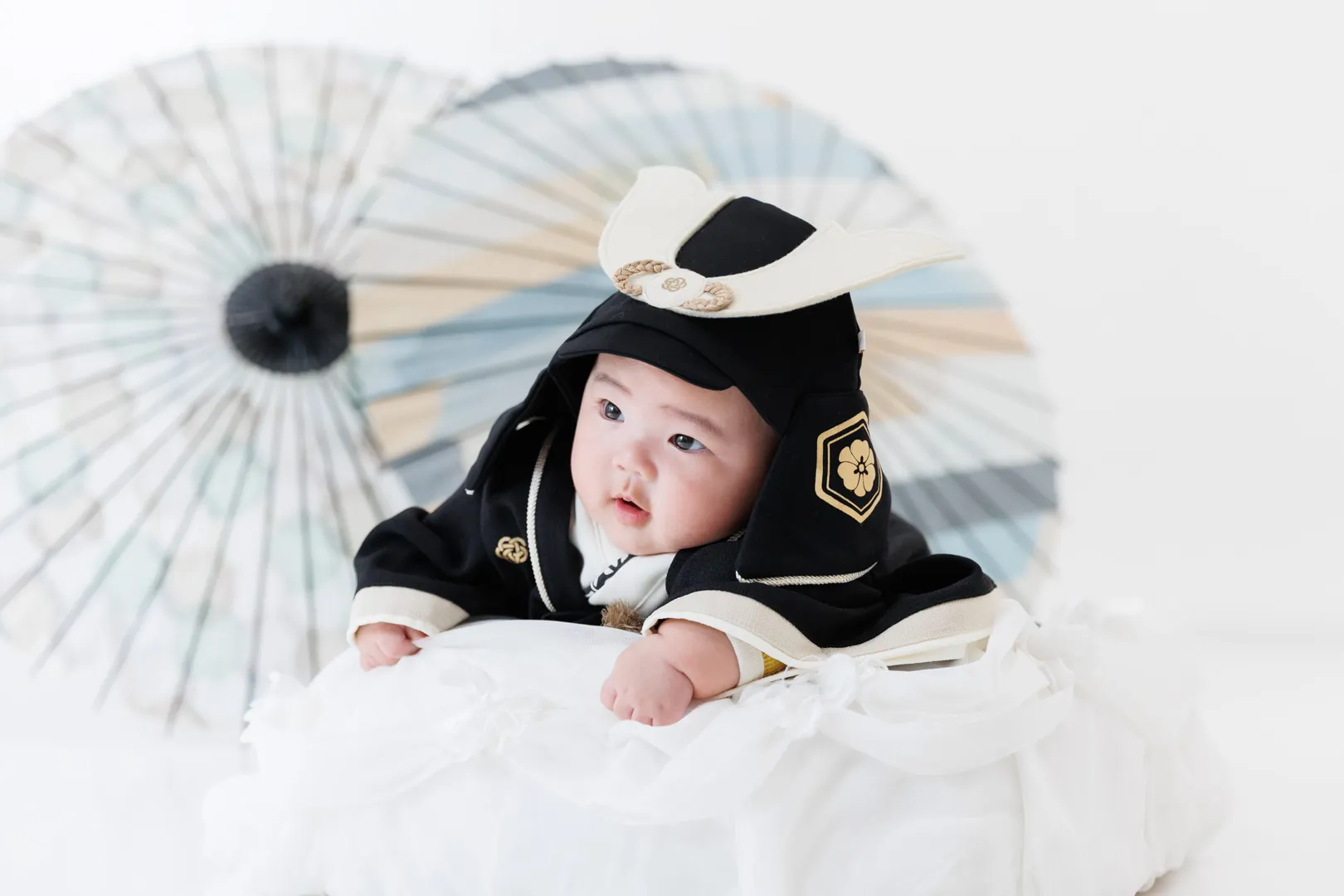 黒と金の伝統的なお宮参り着を着て和傘を背景に寝そべる赤ちゃんのお宮参りフォト（珠洲市）｜ヤマダフォト