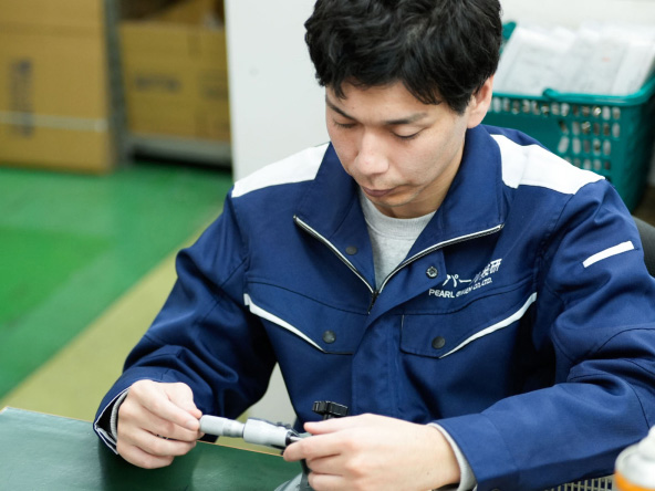 橋本さんが部品を手に持ち作業台で確認している様子