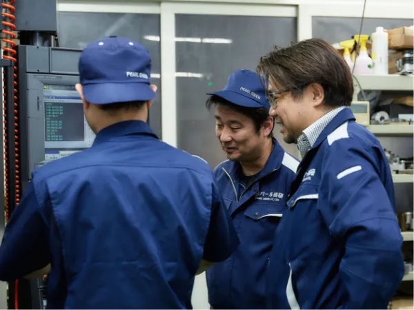 工場内で加工機を前に作業内容を確認するパール技研の社員