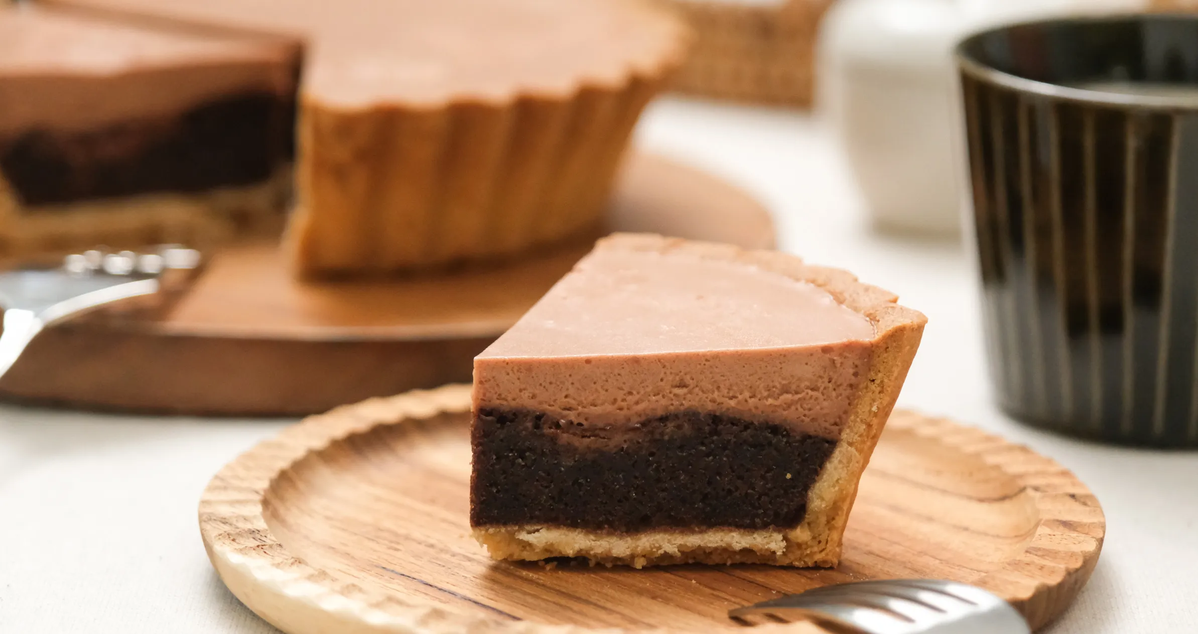 カットされた2層のチョコレートタルトが木製のお皿に置かれ、奥にはホールのタルトが置かれている様子