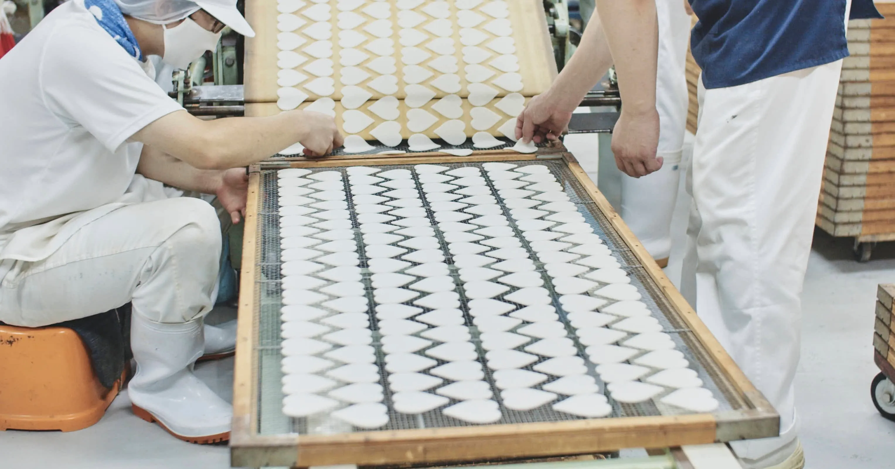 ハート形の生地を網目のトレイに並べる工場の作業員たち