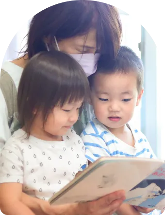 少人数で絵本の読み聞かせをする先生と園児（一人ひとりと向き合える保育） 