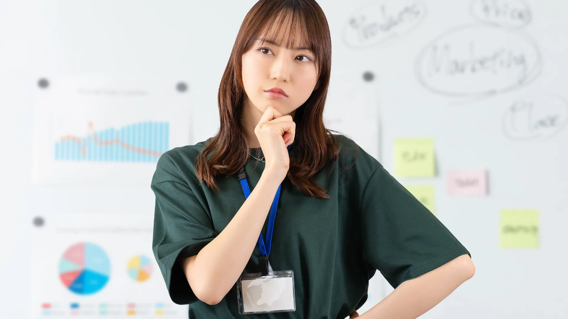 グラフやチャートが書かれたホワイトボードの前で、顎に手を当てて考え込むビジネスパーソン。