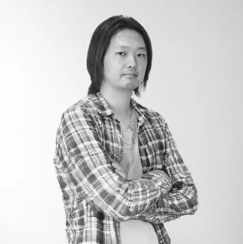 長谷川誠のプロフィール写真。チェック柄のシャツを着て腕を組み、背景はシンプルな白。