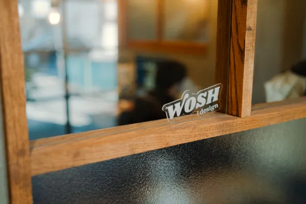 室内の仕切り窓に立てかけられた、WOSH designロゴの小さなアクリルキーホルダー