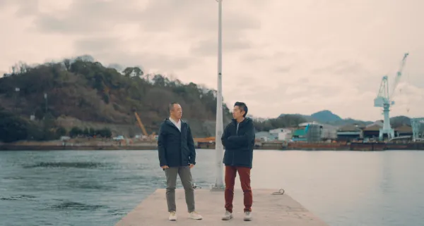  ALTはじまり：二人の男性が水辺の桟橋に立っている様子。左側に代表取締役CEOの野口和央、右側にアートディレクター/デザイナーの溝口耕太が立ち、お互いの顔を見ながら話をしている。ALTおわり