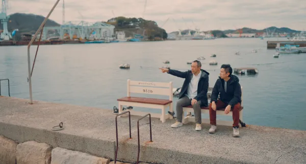  ALTはじまり：尾道水道を背に、野口さんと溝口さんが港にあるベンチに座って話している。野口さんは、対岸を指差して何かを説明している様子。ALTおわり