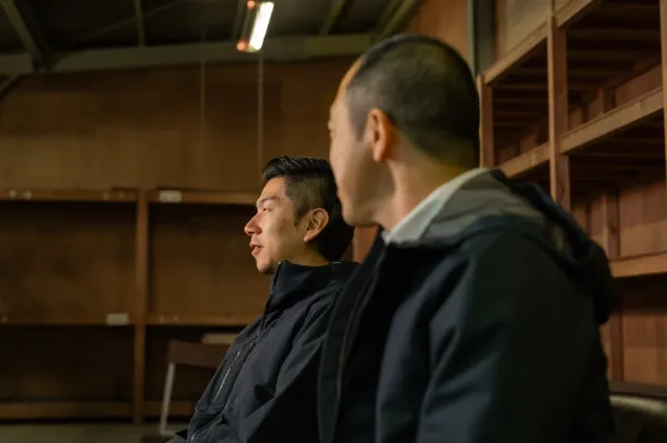 ALTはじまり：座った野口さんが手前に座り、奥に座る溝口さんの方向を向いている。二人とも黒いダウンジャケットを着ている。ALTおわり